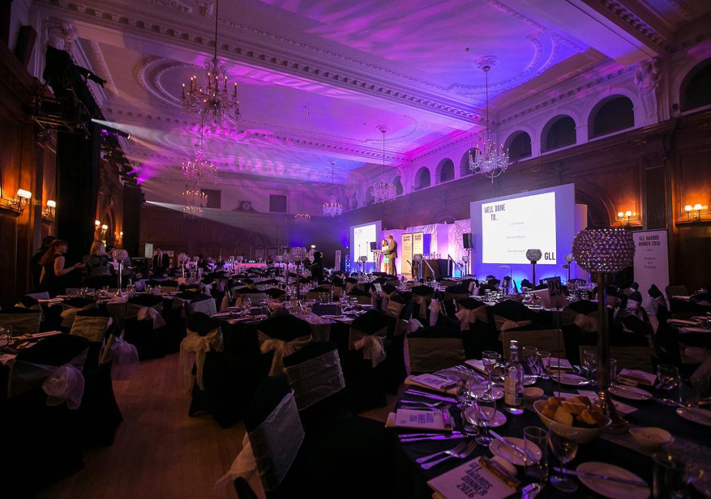 Corporate awards dinner set up in a grand event venue with stage, projection screens, professional lighting and audiovisual production.
